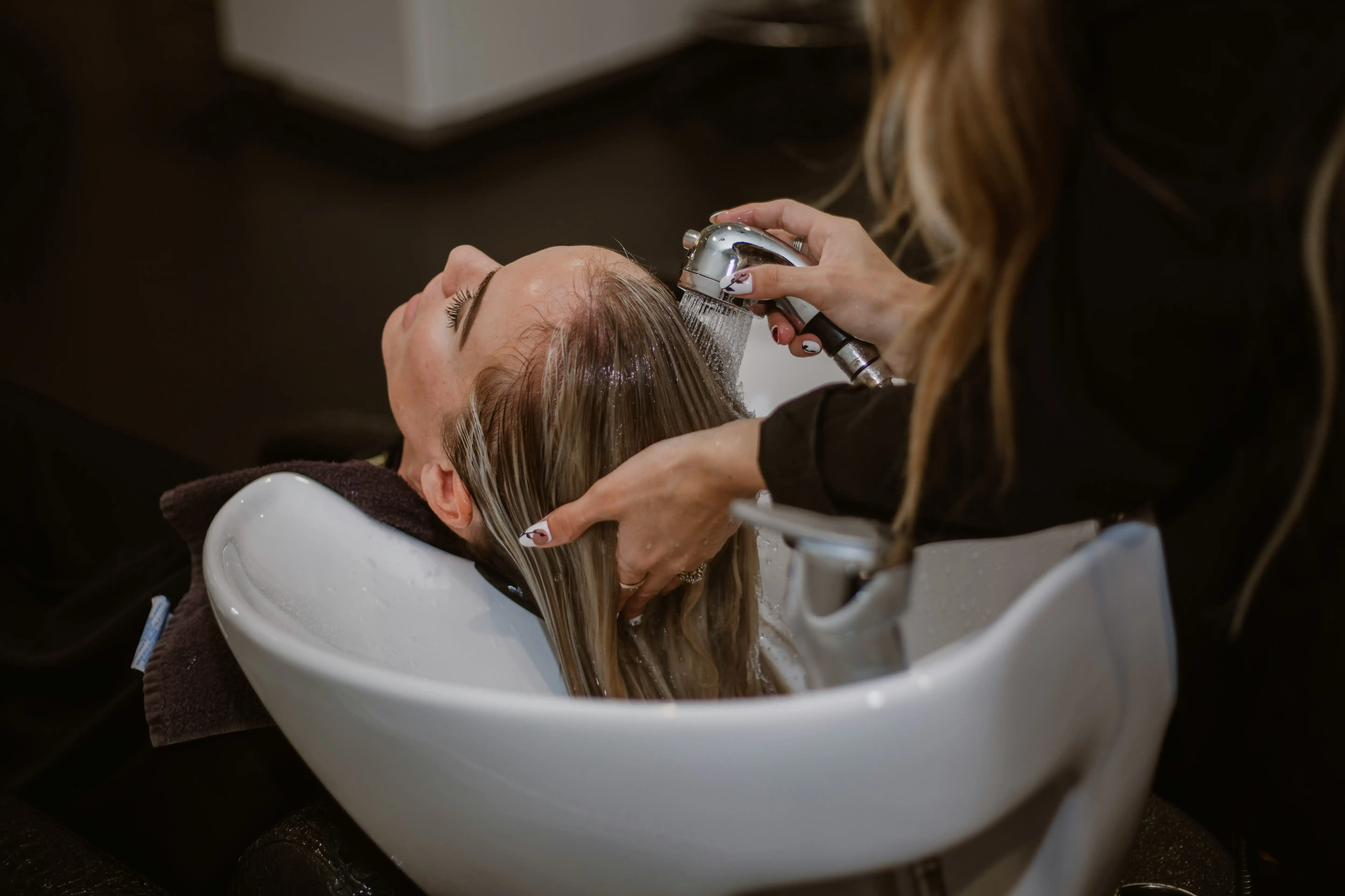 Hair salon service with client reclining as stylist rinses hair at professional sink.