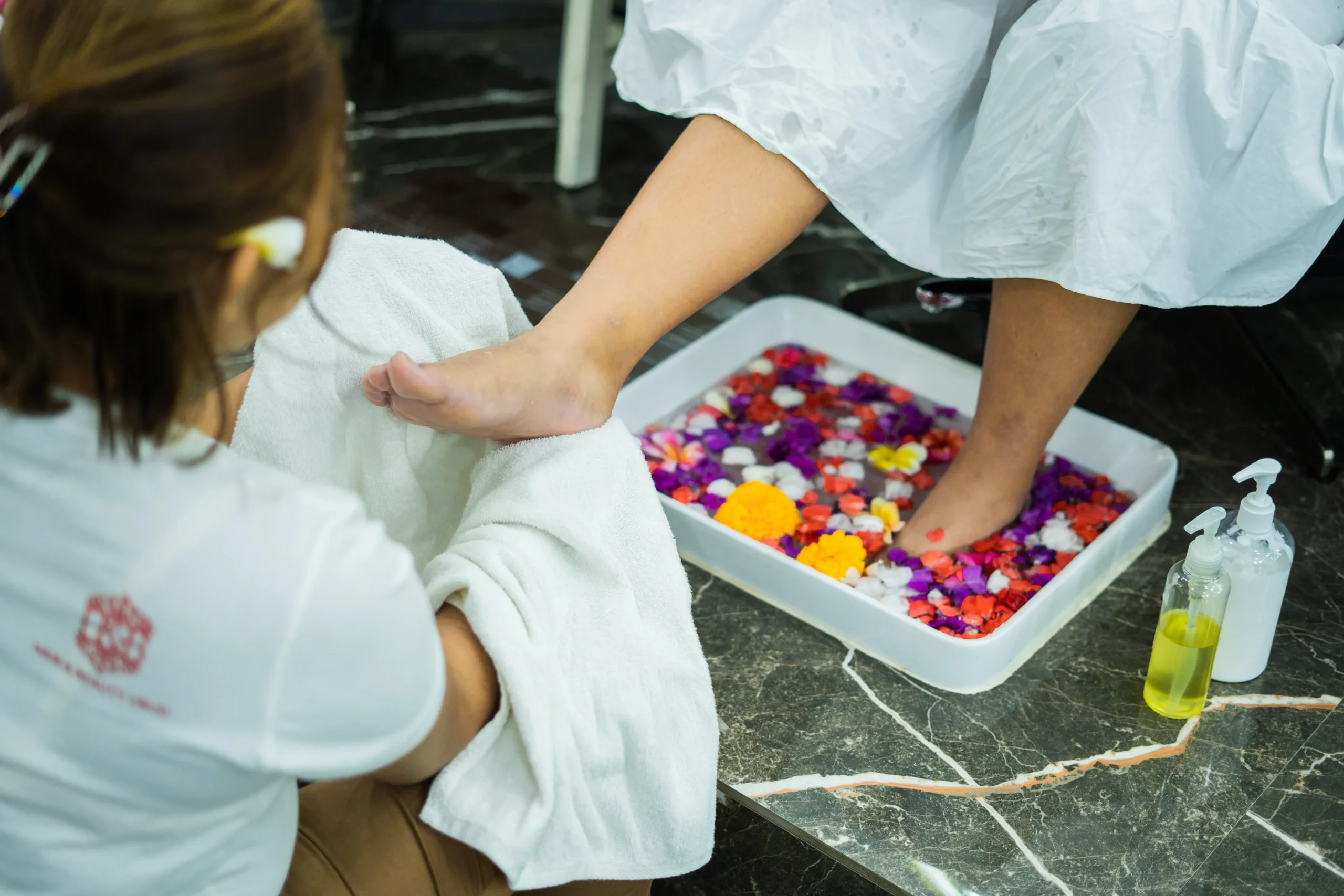 Ubud beauty treatment with therapist drying foot after floral soak in spa basin for relaxation.