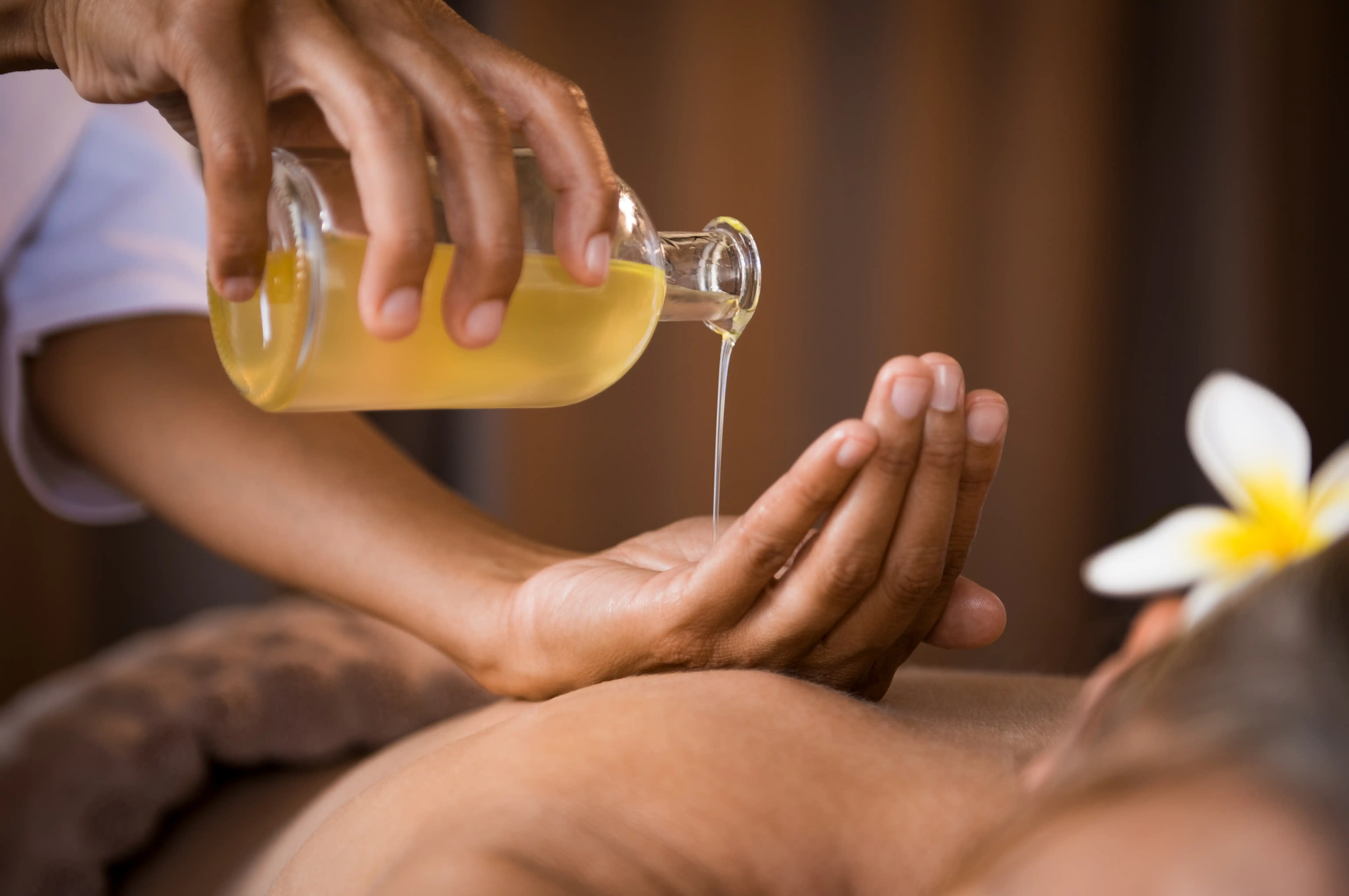 Spa massage session with therapist pouring oil into hand before applying to client’s back.