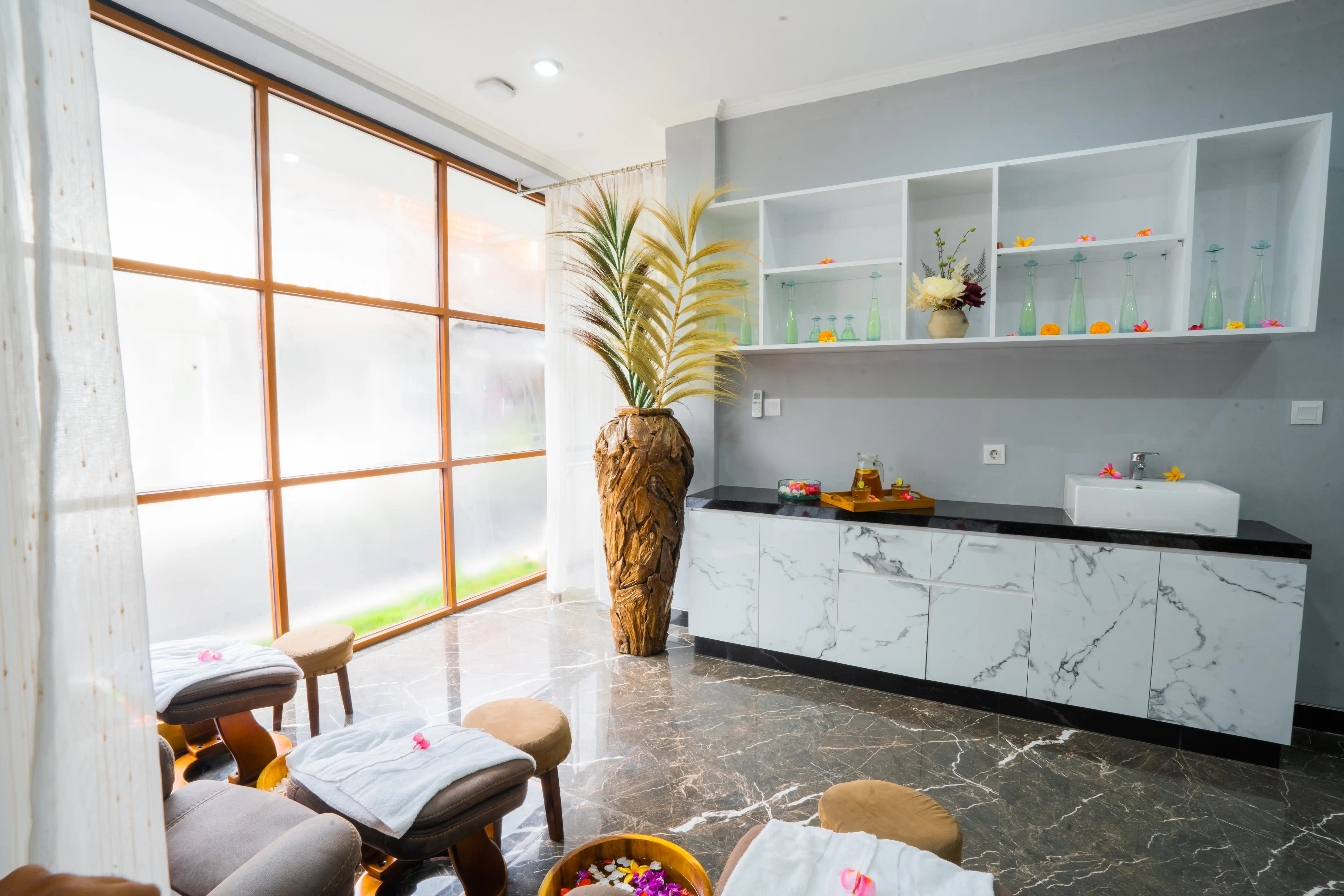 Modern spa relaxation room with flower foot soak, padded chairs, and serene natural light.