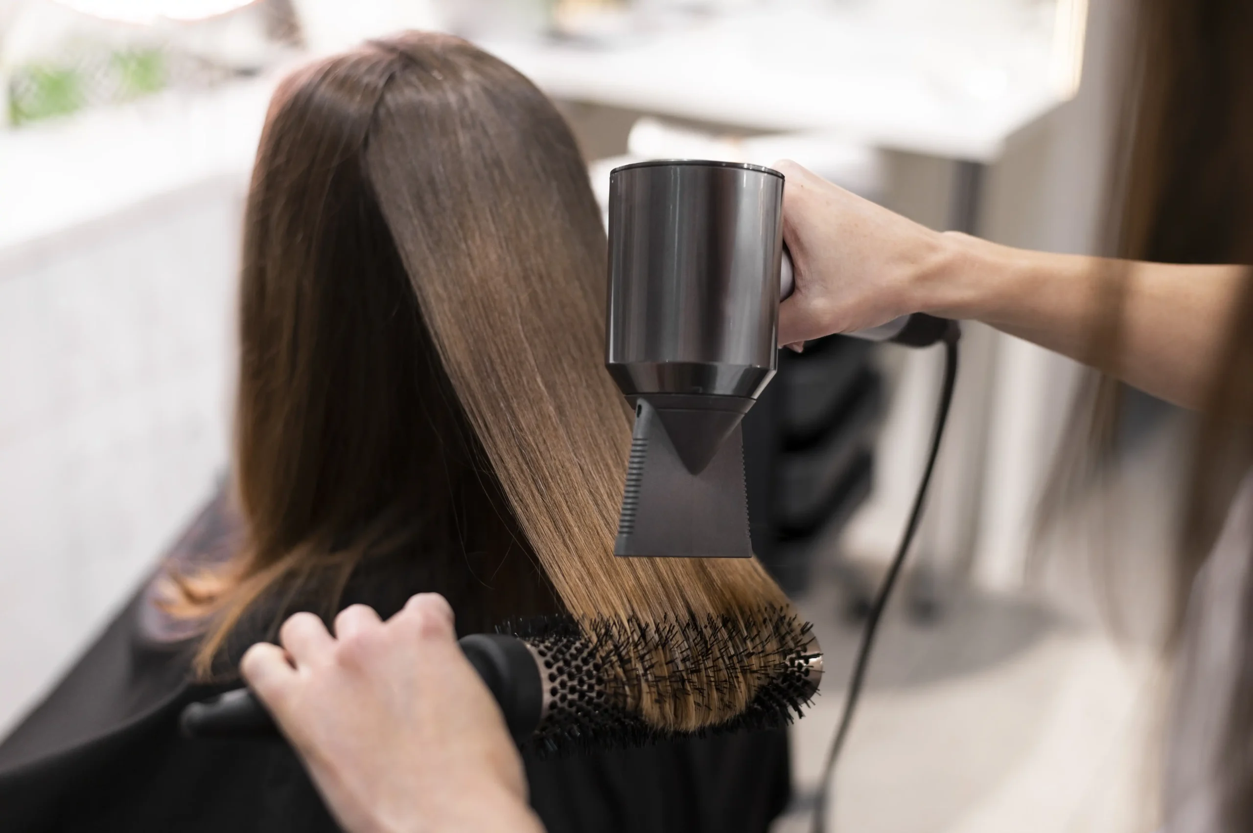 Hair colouring in Ubud salon with stylist blow‑drying and brushing freshly styled brown hair.
